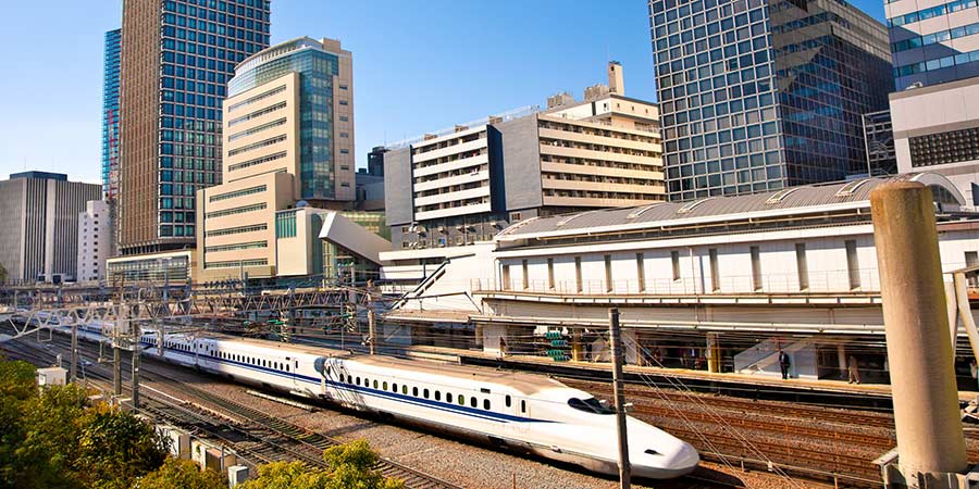 Japan’s bullet train sits at the station with modern skyscrapers towering over it. 